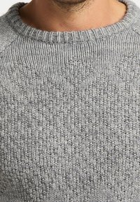 Maglione grigio in maglia con un motivo testurizzato a forma di diamante, scollatura a girocollo e polsini a coste. Il materiale è morbido e confortevole.