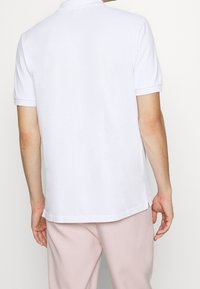 Weißes Poloshirt mit kurzen Ärmeln, umgeschlagenem Kragen, seitlichen Schlitzen am Saum und einer glatten Stofftextur. Entworfen für die Freizeit.