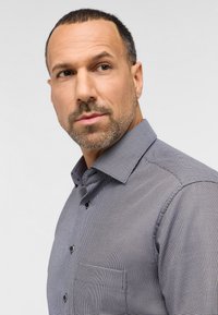 Graues Button-up-Hemd mit einem kleinen geometrischen Muster, Kragen und Brusttasche. Der Stoff wirkt glatt und hat eine taillierte Passform.