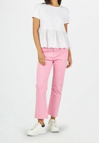 Haut blanc à manches courtes avec un ourlet en dentelle, associé à un pantalon rose. Des baskets blanches complètent la tenue. Le tissu semble doux avec un détail texturé.