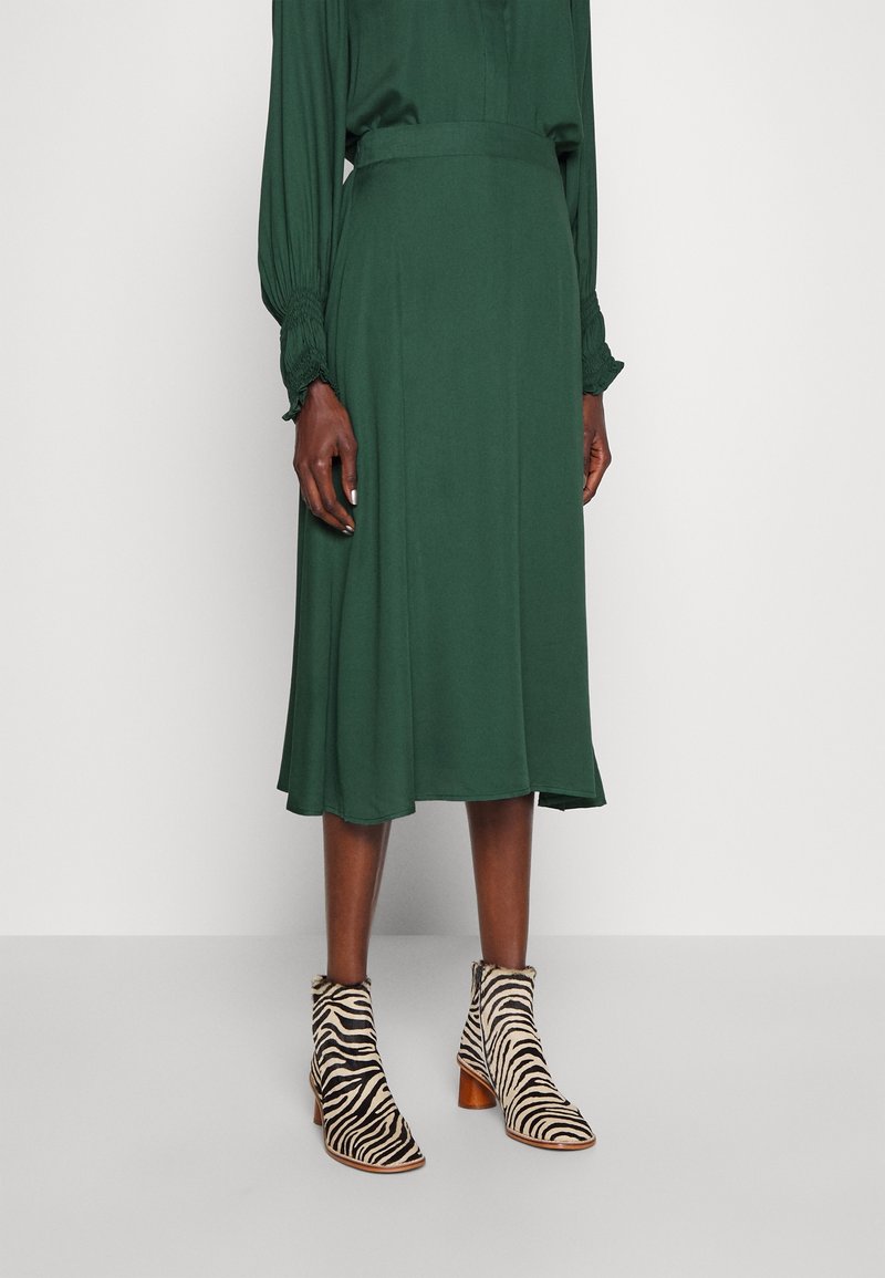 Groene midi-rok met een gladde textuur, gecombineerd met enkelboots in zebra-print met een blokhak en zachte faux fur afwerking.