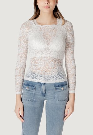 Top de encaje blanco de manga larga con patrón floral, escote ondulado, diseño ajustado, combinado con jeans de color azul claro. Incluye detalles de bolsillos.