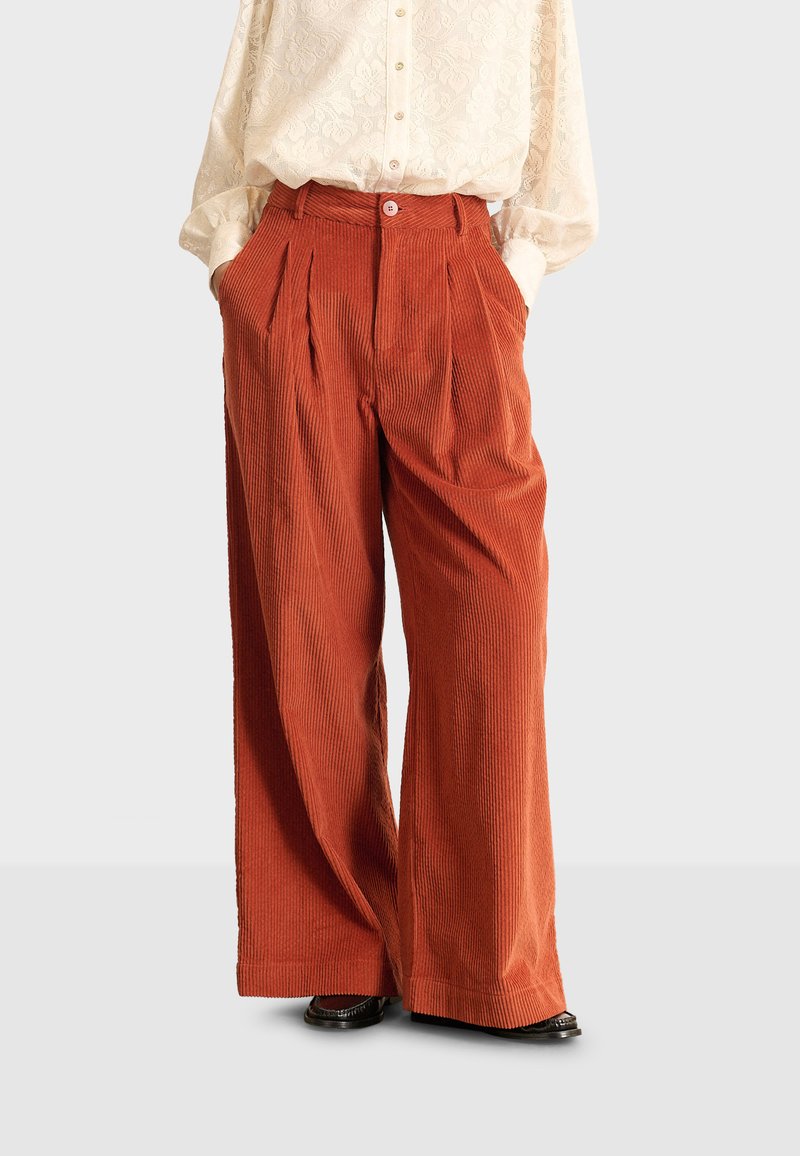 Pantaloni in corda a gamba larga di colore arancio bruciato con righe verticali, dotati di pieghe frontali e una vita aderente con chiusura a bottone.