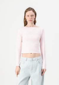 Lyse rosa langermet cropped topp med et dekorativt "Hugo"-logo i sølv. Glatt tekstur, enkelt design og båt halsstil.
