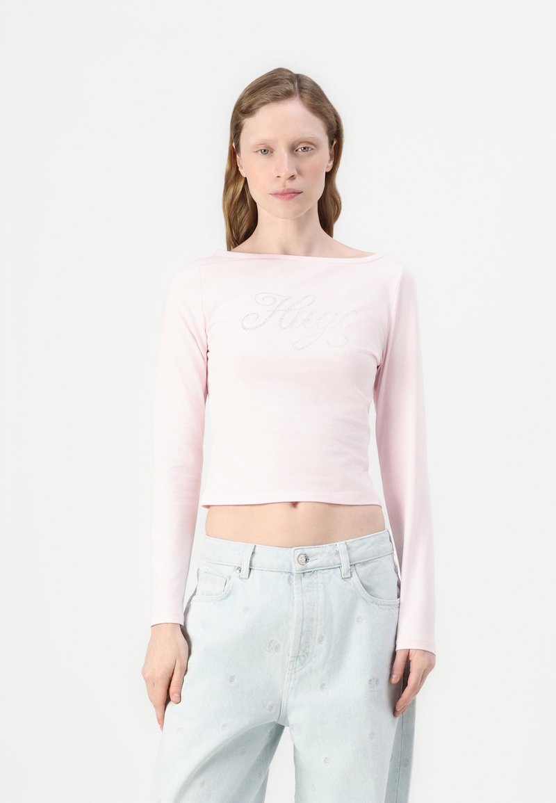 Lyse rosa langermet cropped topp med et dekorativt "Hugo"-logo i sølv. Glatt tekstur, enkelt design og båt halsstil.