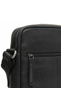 Borsa in pelle nera con forma rettangolare, caratterizzata da una texture liscia, chiusura con zip superiore, tasca frontale e dettagli in metallo.