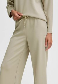 Pantalones de pierna ancha en beige claro con cintura ajustable. Textura suave, corte relajado y detalles de diseño mínimos. Adecuados para uso casual.