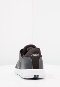 Baskets de sport noires avec une tige en mesh texturé, des accents en cuir lisse, un col rembourré et une semelle en caoutchouc blanche. Présente un branding Lacoste.