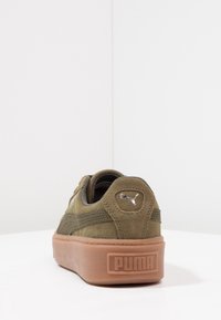Olivově zelené semišové tenisky s texturovaným povrchem, s hnědou gumovou podrážkou a stříbrným logem Puma na patě. Nízký střih.