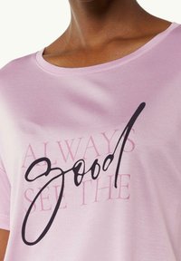 Camiseta de algodón rosa claro con cuello redondo y texto en cursiva negra "good" con la frase "ALWAYS SEE THE" impresa en un rosa más claro.