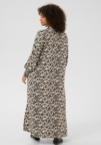 Robe longue et fluide à motif losange noir et crème, dotée de manches longues et d'un col rond. Tissu texturé avec une silhouette fluide.