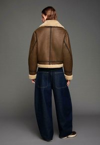 Brown leren bomberjack met een crèmekleurige shearling kraag en manchetten, gecombineerd met wijde donkerdenim jeans.