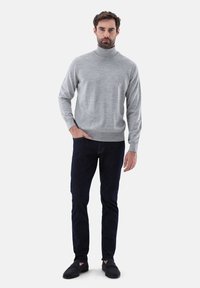 Grauer Rollkragenpullover aus weichem Stoff, mit taillierter Silhouette, kombiniert mit dunklen Jeans und schwarzen Slipschuhen.