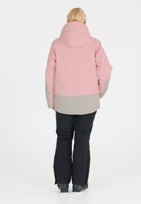 Rosa und graue Winterjacke mit Kapuze, kombiniert mit schwarzen Schneehosen. Die Jacke hat ein Farbblock-Design und eine lockere Passform.
