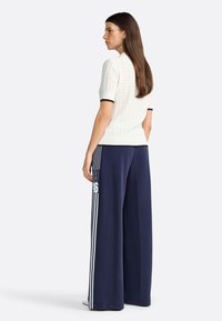 Haut en tricot blanc à manches courtes avec un motif texturé, associé à un pantalon ample bleu marine avec des rayures verticales blanches et des accents numériques.
