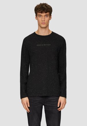 Zwarte lange mouwen shirt met een gemêleerd patroon, ronde halslijn en subtiele tekstdetails aan de voorkant. Gepaard met donkere jeans.