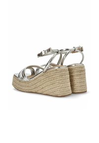 Sandalias de cuña con parte superior de metal plateado, diseño de múltiples correas y suela de yute trenzado con un acabado natural texturizado. Cierre con hebilla visible.