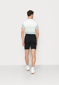 Helles grünes und weiß gestreiftes T-Shirt mit schwarzen Shorts. Das T-Shirt hat kurze Ärmel und einen Rundhalsausschnitt. Die Shorts haben eine glatte Textur und einen elastischen Bund.