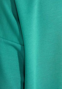 Gros plan d'un tissu bleu-vert montrant la texture tricotée et les plis de couture.