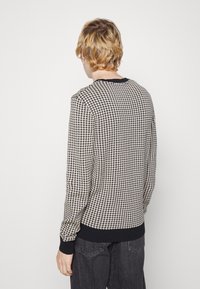 Knit sweater in black and cream houndstooth pattern, featuring a round neckline and ribbed cuffs. Soft texture, fitted silhouette.