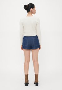 Kremfarget ribbestrikket genser og mørkeblå denimshorts med fem lommer, med kontrasterende sømmer. Brune ankelstøvletter med hæl fullfører antrekket.