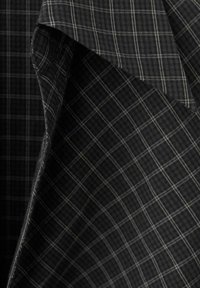 Tela a cuadros en blanco y negro con finas líneas blancas, que muestra una textura suave y un corte diagonal, sugiriendo versatilidad en el diseño.