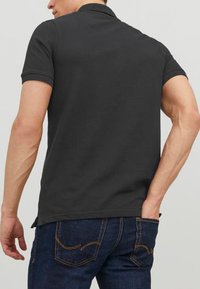 Mørkegrå polo-shirt med korte ærmer og krave, båret med blå denimbukser med gul søm på lommerne.