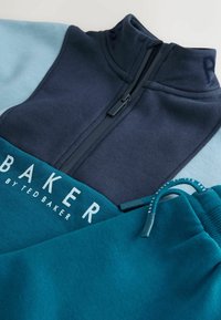 Sudadera de medio cremallera y joggers a juego en azul marino y azul teal, con tejido suave, detalle del logo y cordón ajustable en los pantalones.