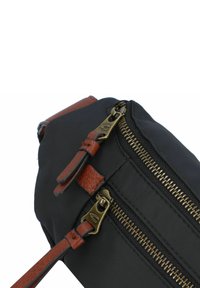 Zwarte stoffen tas met bronzen ritsen, bruin leren accenten en een platte vorm. Beschikt over twee ritscompartimenten en een verstelbare schouderband.