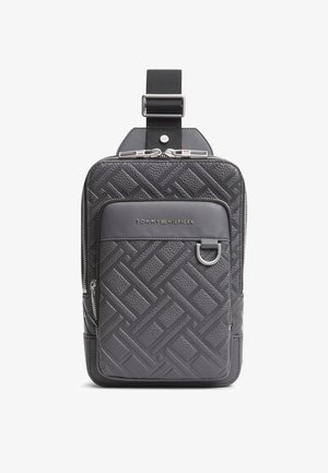 Kompaktowa czarna torba na ramię z tłoczonym geometrycznym wzorem, przednią kieszenią na suwak, metalowym kółkiem D oraz logo Tommy Hilfiger na górze przodu.