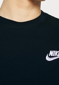Camiseta de algodón negra con cuello redondo acanalado y un logo de Nike bordado en blanco en el lado izquierdo del pecho, textura suave.