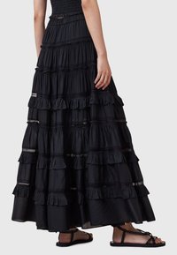 Jupe maxi noire à volants superposés avec des détails en dentelle. Tissu léger, taille élastique, portée avec des sandales noires.