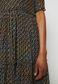 Musta kukkamekko, jossa on tiukka vartalo ja kerrostettu hame, pieniä monivärisiä kukkapainatuksia ja teksturoitu, kevyt kangas.