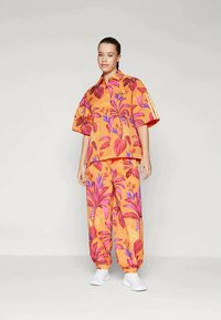 Ογκώδης μπλούζα με πορτοκαλί λουλούδια και ταιριαστά παντελόνια με ροζ και μωβ λεπτομέρειες, διαθέτοντας χαλαρή εφαρμογή και κα casual σχεδίαση.