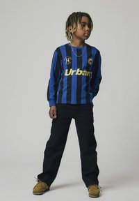 Camisa de manga larga a rayas en azul y negro con "Urban" en dorado, combinada con pantalones negros y zapatos marrones. Presenta un logo en el pecho.
