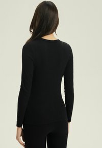 Czarna, długoszczynowa koszula wykonana z ryflowanej tkaniny. Posiada okrągły dekolt oraz dopasowany krój. Noszona z dopasowanymi czarnymi spodniami.