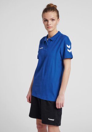Blue polo shirt made of cotton with a collar, featuring white chevron patterns on sleeves and a logo on the chest. Paired with black shorts.