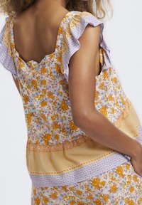 Top con estampado floral en amarillo, púrpura y blanco; cuenta con mangas con volantes; diseño floral con acentos en naranja y azul, textura suave.