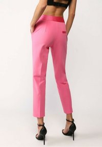 Vaaleanpunaiset räätälöidyt housut, joissa on sileä pinta, lyhyt pituus ja takataskut; erotuksena punainen vyötärönauha ja kapea istuvuus.