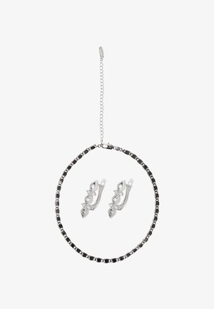 Collar plateado con diseño de cadena circular y detalles negros; incluye pendientes a juego con un giro decorativo y piedras preciosas claras.