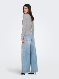 Langærmet top med hvide og sorte striber, kombineret med oversized lyseblå denimjeans. Har en afslappet pasform og minimalistisk design.
