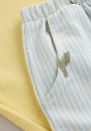 Žlutá bavlněná tkanina vedle světle modrých bavlněných kalhot s vertikálními pruhy a malým šedým detailem u kapsy. Ležérní, jemné textury.
