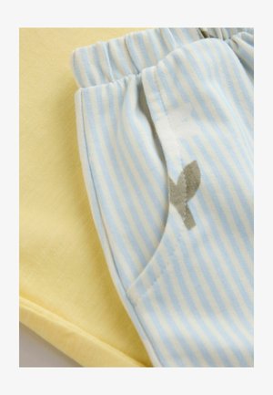 Żółty bawełniany materiał obok jasnoniebieskich, pionowo prążkowanych bawełnianych spodni z małym szarym akcentem przy kieszeni. Swobodne, miękkie tekstury.