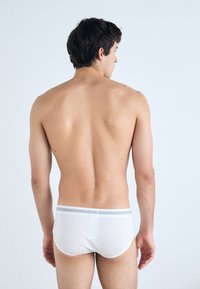 Weiße Baumwollunterhosen mit einem grauen gestreiften Bund, von hinten betrachtet. Glatte Textur und taillierte Passform, die die Taille und Beine betont.