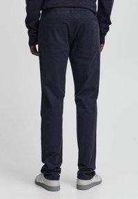 Navy cotton pants with a straight-leg design, two back pockets featuring stitching details, worn with gray sneakers.