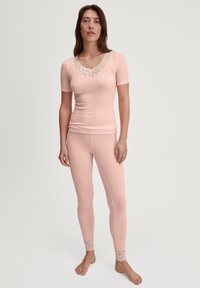 Vrouw in een bijpassende lichtroze ribbel top met korte mouwen en legging set met witte kanten rand bij de halslijn en de boorden van de leggings, blootsvoets.