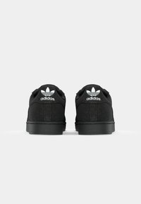 Crne tenisice s gornjim dijelom od teksturirane tkanine, ravnim vezicama i gumenim potplatima. Imaju bijeli Adidas logo i dizajn s tri pruge na stražnjem dijelu.