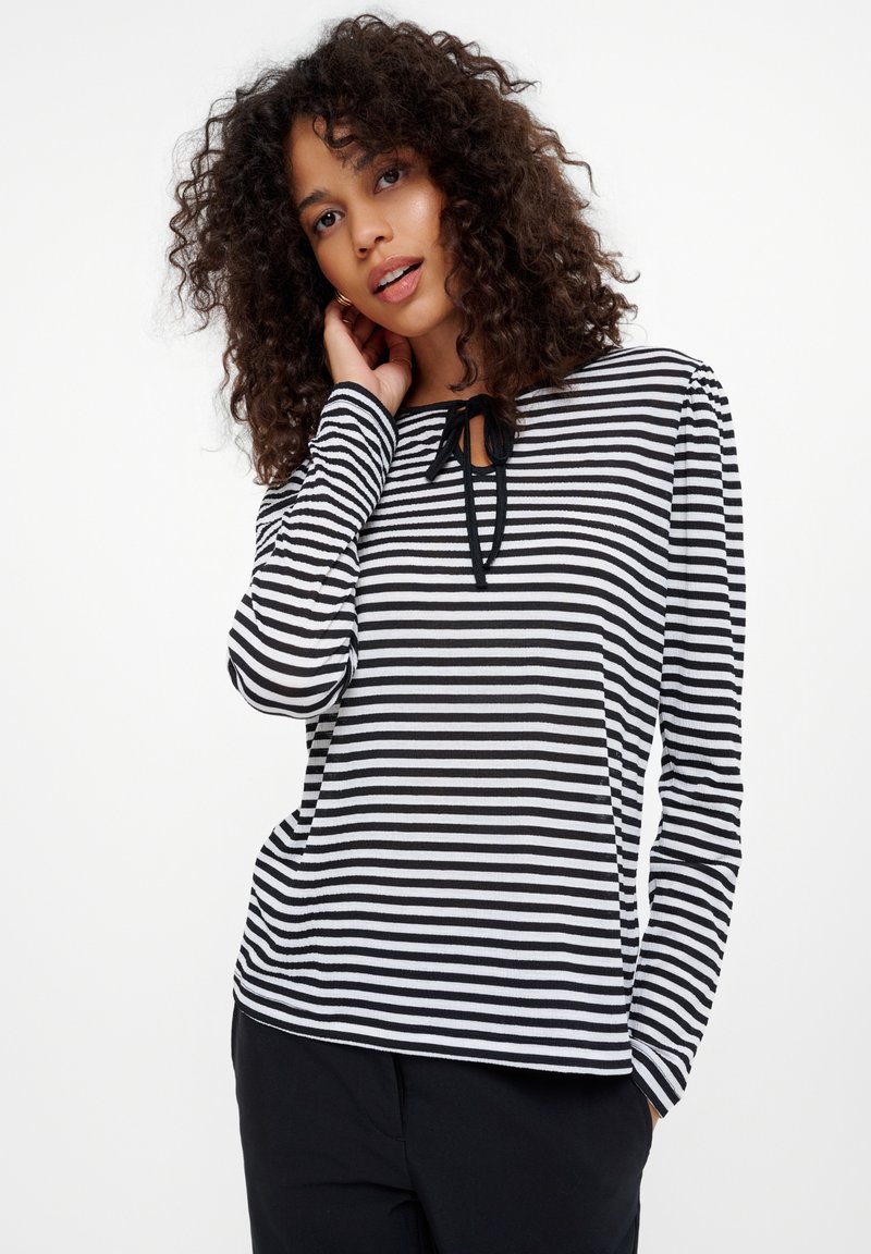 Czarna i biała, w paski, bluzka z długim rękawem z okrągłym dekoltem, z małym detalem w postaci kokardy z przodu oraz teksturowanym materiałem.