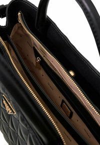 Sac à main noir matelassé avec un extérieur lisse, une quincaillerie dorée et un intérieur beige avec un motif de logo. Compartiments zippés inclus.