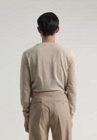 Suéter de punto beige de manga larga con cuello redondo, combinado con pantalones beiges a medida que tienen bolsillos traseros y acentos laterales.